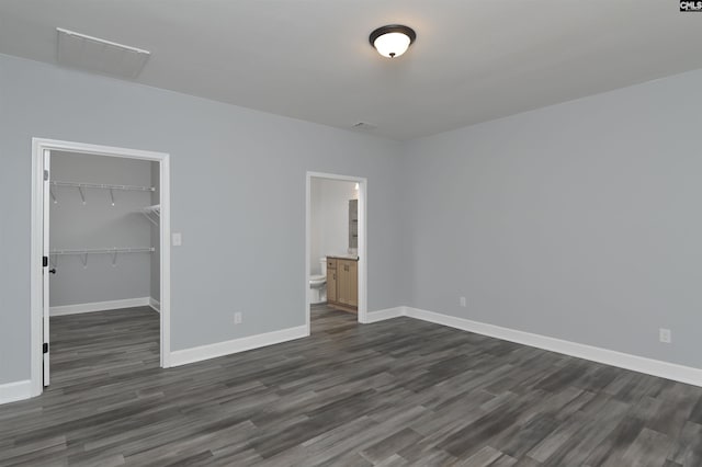 unfurnished bedroom with ensuite bath, a spacious closet, dark hardwood / wood-style flooring, and a closet