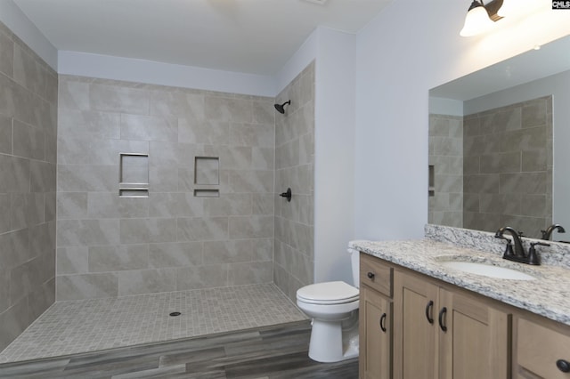 bathroom with hardwood / wood-style flooring, vanity, tiled shower, and toilet