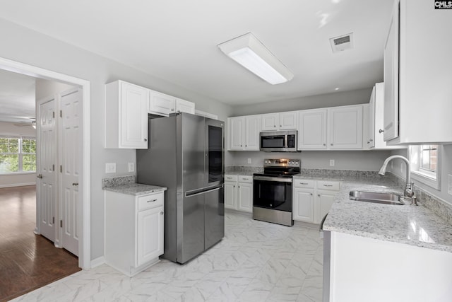 kitchen featuring appliances with stainless steel finishes, sink, white cabinets, ceiling fan, and light stone countertops