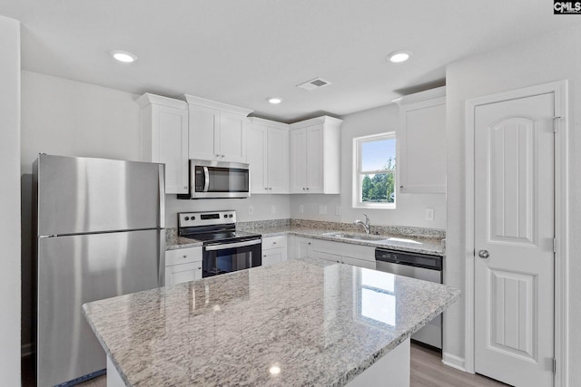 kitchen featuring stainless steel appliances, white cabinetry, a kitchen island, and sink