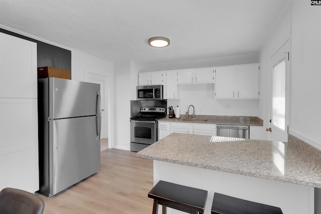 kitchen featuring a breakfast bar, sink, appliances with stainless steel finishes, light hardwood / wood-style floors, and white cabinets