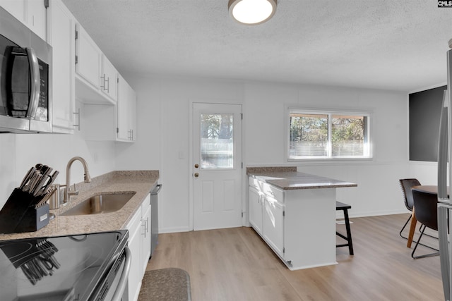 kitchen featuring sink, light hardwood / wood-style flooring, a breakfast bar, appliances with stainless steel finishes, and white cabinetry