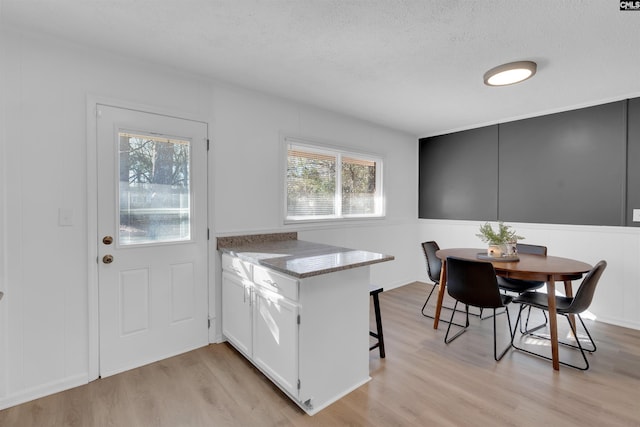 kitchen featuring a kitchen bar, light hardwood / wood-style floors, white cabinets, and stone counters