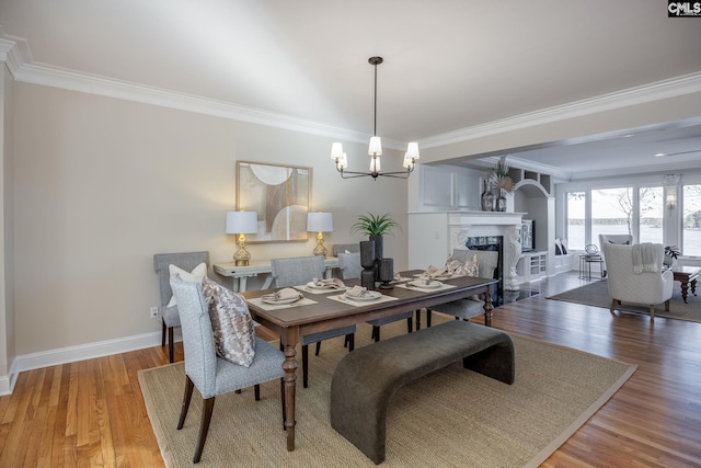 dining area with a notable chandelier, crown molding, wood-type flooring, and a premium fireplace