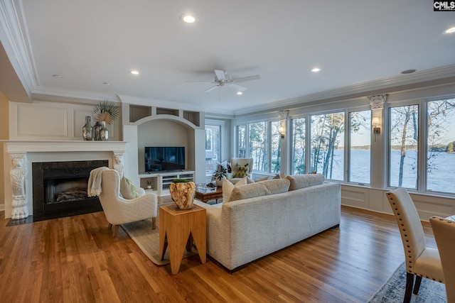 living room with crown molding, ceiling fan, wood-type flooring, and a fireplace