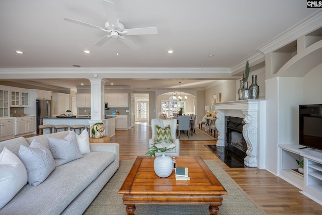 living room with crown molding, a high end fireplace, light hardwood / wood-style floors, and ceiling fan with notable chandelier