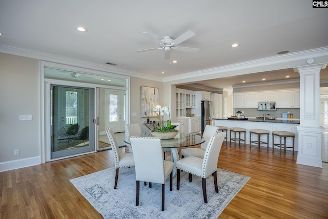 dining space featuring crown molding, light hardwood / wood-style flooring, decorative columns, and ceiling fan