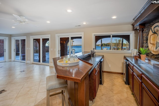 kitchen featuring light tile patterned flooring, a kitchen bar, a water view, a kitchen island, and ceiling fan