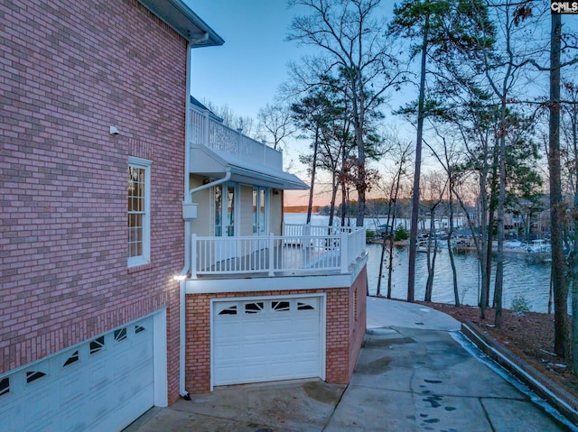 property exterior at dusk featuring a water view, a balcony, and a garage