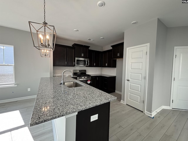 kitchen featuring light wood finished floors, appliances with stainless steel finishes, a sink, and light stone counters