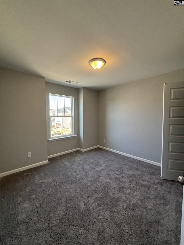 spare room featuring baseboards, visible vents, and dark carpet