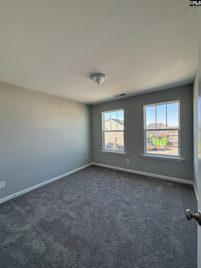 spare room with dark colored carpet, visible vents, and baseboards