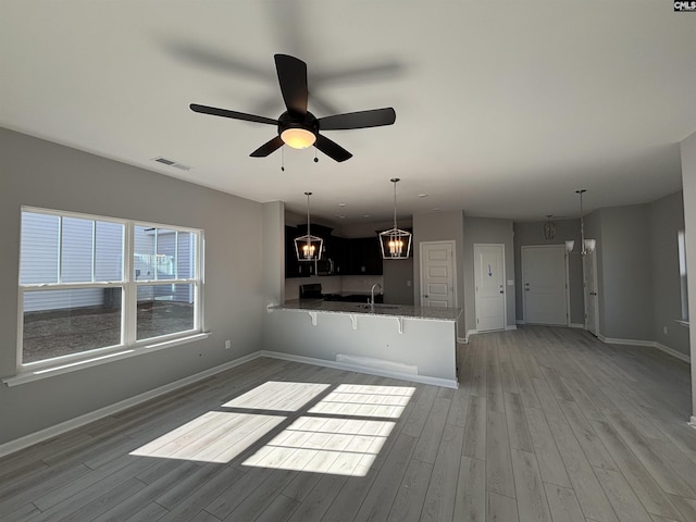 unfurnished living room with light wood finished floors, baseboards, visible vents, a sink, and ceiling fan with notable chandelier