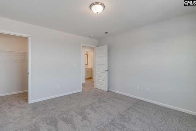 unfurnished bedroom with light carpet, a walk in closet, and a closet