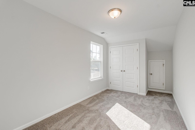 unfurnished bedroom featuring a closet, lofted ceiling, and light carpet