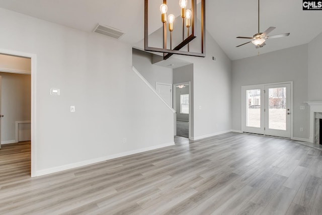 unfurnished living room featuring ceiling fan with notable chandelier, a fireplace, high vaulted ceiling, and light hardwood / wood-style flooring