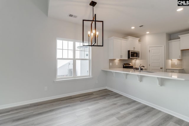 kitchen with sink, a breakfast bar area, appliances with stainless steel finishes, white cabinetry, and decorative light fixtures