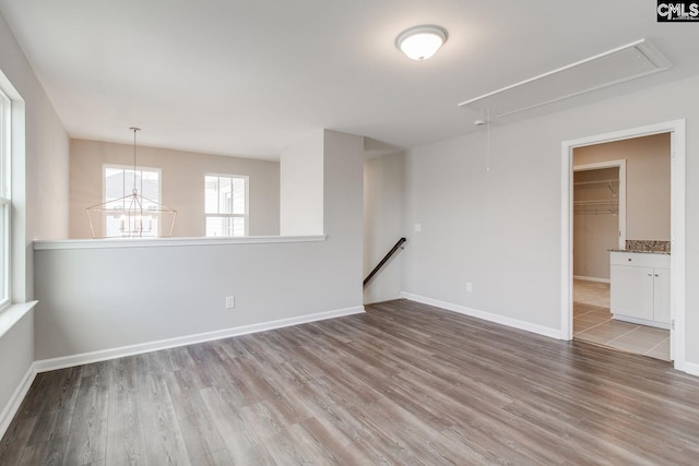 spare room featuring attic access, a chandelier, baseboards, and wood finished floors