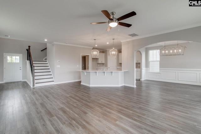 unfurnished living room featuring arched walkways, ceiling fan with notable chandelier, wood finished floors, visible vents, and stairway