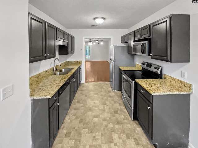 kitchen featuring sink, ceiling fan, appliances with stainless steel finishes, light stone counters, and a textured ceiling