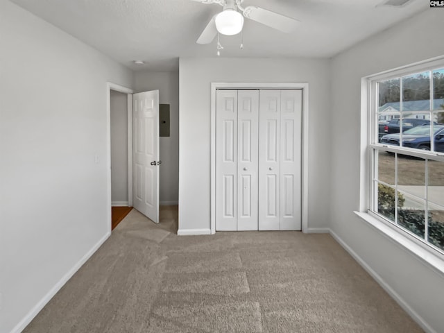 unfurnished bedroom with ceiling fan, electric panel, light colored carpet, and a closet