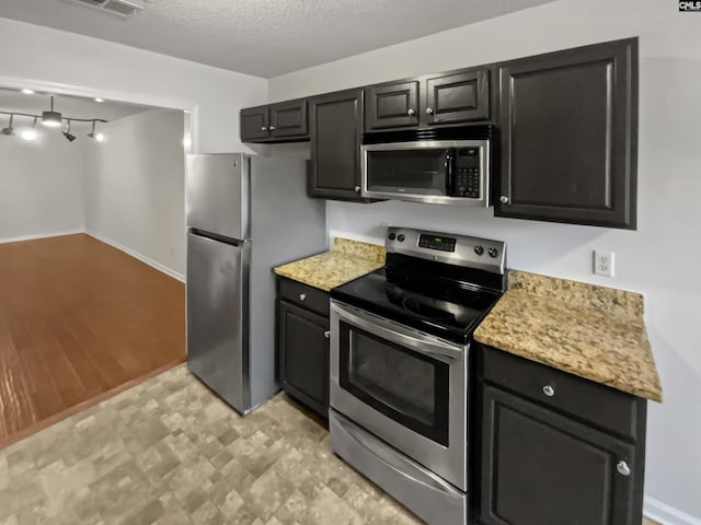 kitchen with stainless steel appliances, light stone countertops, and a textured ceiling