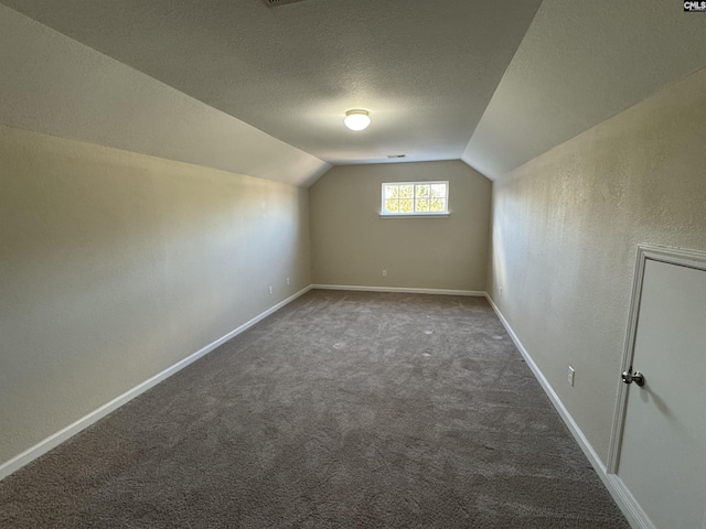 additional living space with dark carpet, vaulted ceiling, and a textured ceiling