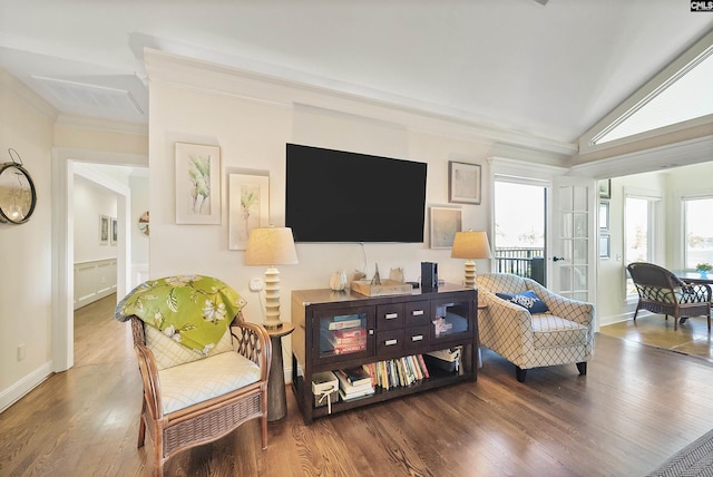 living area with wood-type flooring, ornamental molding, and vaulted ceiling