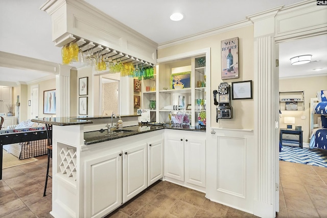 kitchen with dark stone counters, ornamental molding, kitchen peninsula, and white cabinets