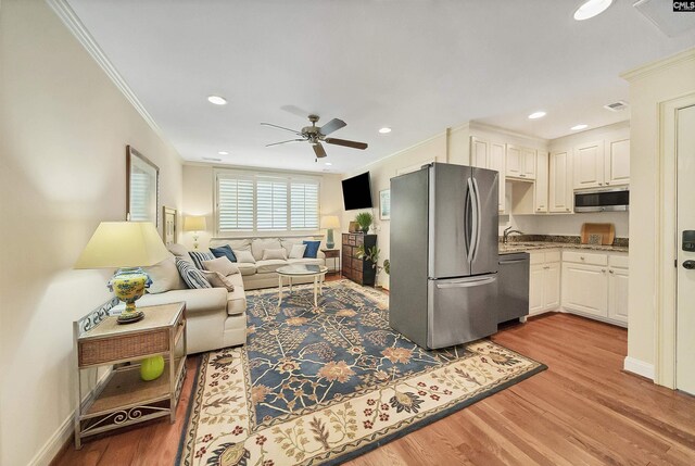 living room with sink, crown molding, light hardwood / wood-style floors, and ceiling fan