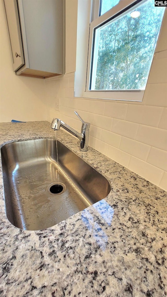 interior details with light stone counters, sink, gray cabinetry, and decorative backsplash