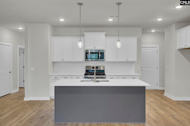 kitchen featuring stainless steel appliances, white cabinetry, a kitchen island with sink, and decorative light fixtures