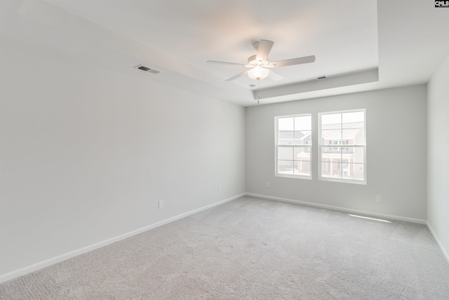 carpeted spare room with a raised ceiling and ceiling fan