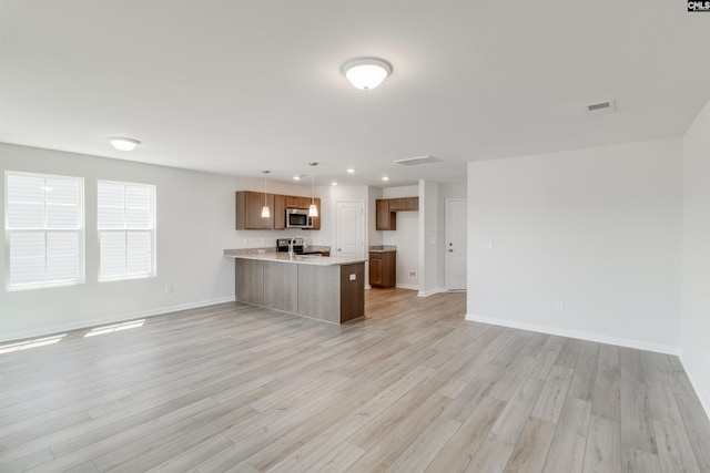 kitchen with decorative light fixtures, light hardwood / wood-style flooring, stainless steel appliances, and kitchen peninsula