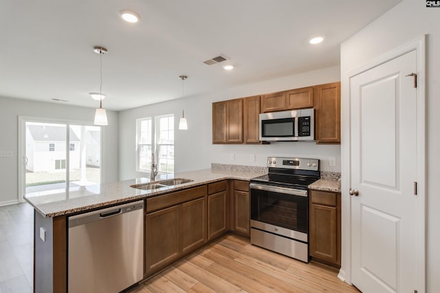 kitchen with sink, light hardwood / wood-style flooring, appliances with stainless steel finishes, kitchen peninsula, and pendant lighting