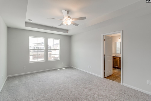 carpeted spare room with a tray ceiling and ceiling fan