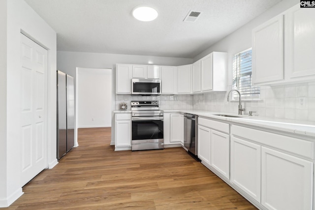 kitchen featuring sink, appliances with stainless steel finishes, white cabinetry, decorative backsplash, and light wood-type flooring