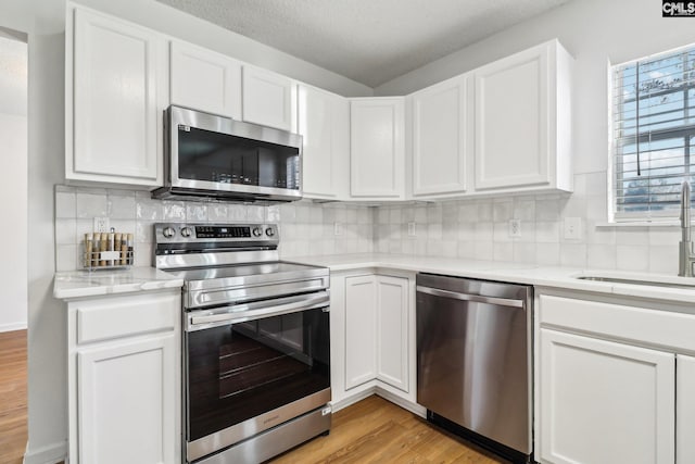 kitchen with sink, white cabinetry, light stone counters, appliances with stainless steel finishes, and light hardwood / wood-style floors