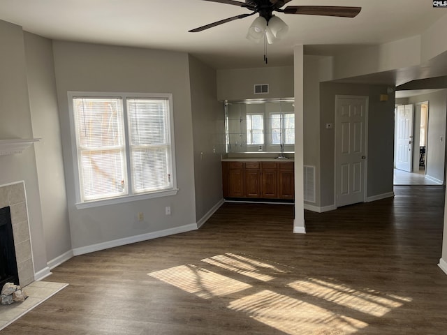 unfurnished living room with a tiled fireplace, dark hardwood / wood-style flooring, plenty of natural light, and ceiling fan