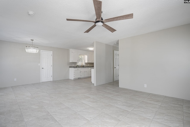 unfurnished living room featuring ceiling fan with notable chandelier, sink, and a textured ceiling