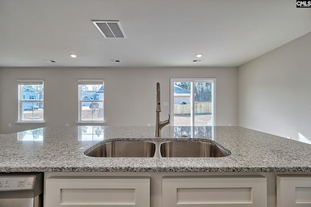 kitchen featuring light stone counters, dishwashing machine, sink, and white cabinets