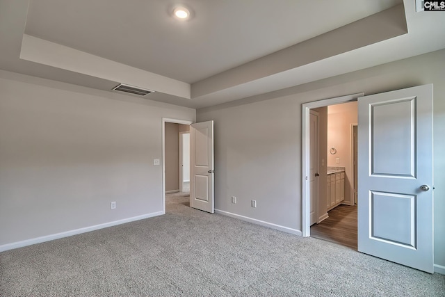 unfurnished bedroom featuring ensuite bath, a tray ceiling, and light colored carpet