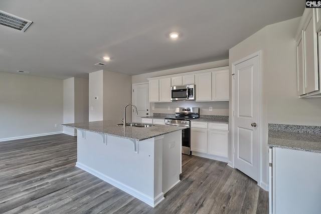 kitchen featuring stone countertops, an island with sink, sink, white cabinets, and stainless steel appliances