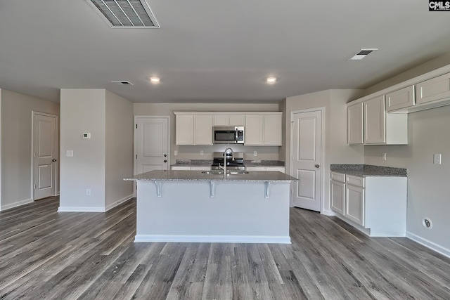 kitchen with light stone countertops, appliances with stainless steel finishes, and a kitchen island with sink