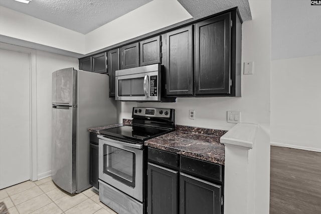 kitchen with light tile patterned floors, a textured ceiling, and appliances with stainless steel finishes