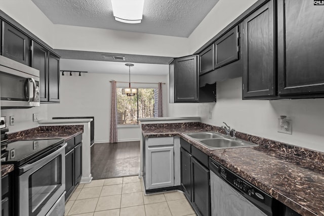 kitchen with appliances with stainless steel finishes, sink, hanging light fixtures, light tile patterned floors, and a textured ceiling