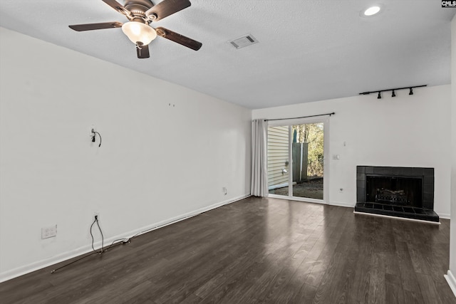 unfurnished living room with a tiled fireplace, dark wood-type flooring, a textured ceiling, and ceiling fan