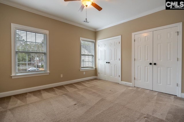 unfurnished bedroom with ceiling fan, light colored carpet, ornamental molding, and two closets