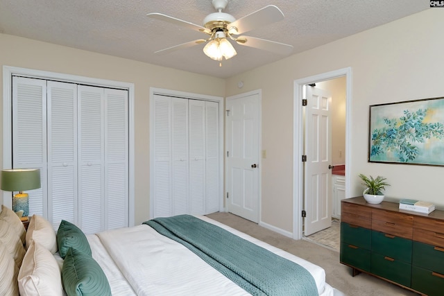 carpeted bedroom with multiple closets, a textured ceiling, and ceiling fan