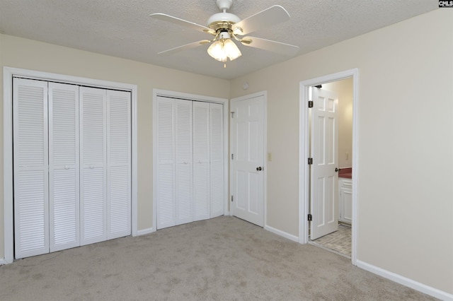 unfurnished bedroom with ensuite bathroom, a textured ceiling, light carpet, two closets, and ceiling fan